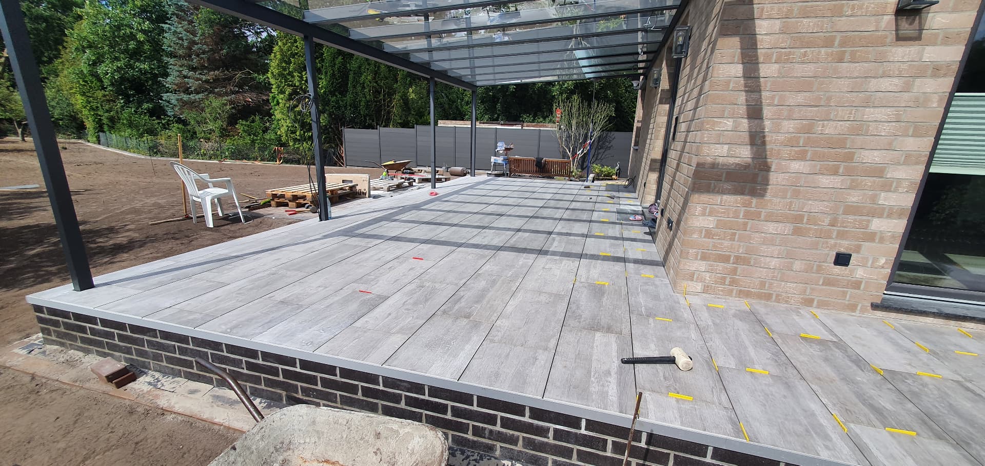 Terrasseneubau in Bremen: Platten mit Holzdekor werden unter der Glasüberdachung verlegt